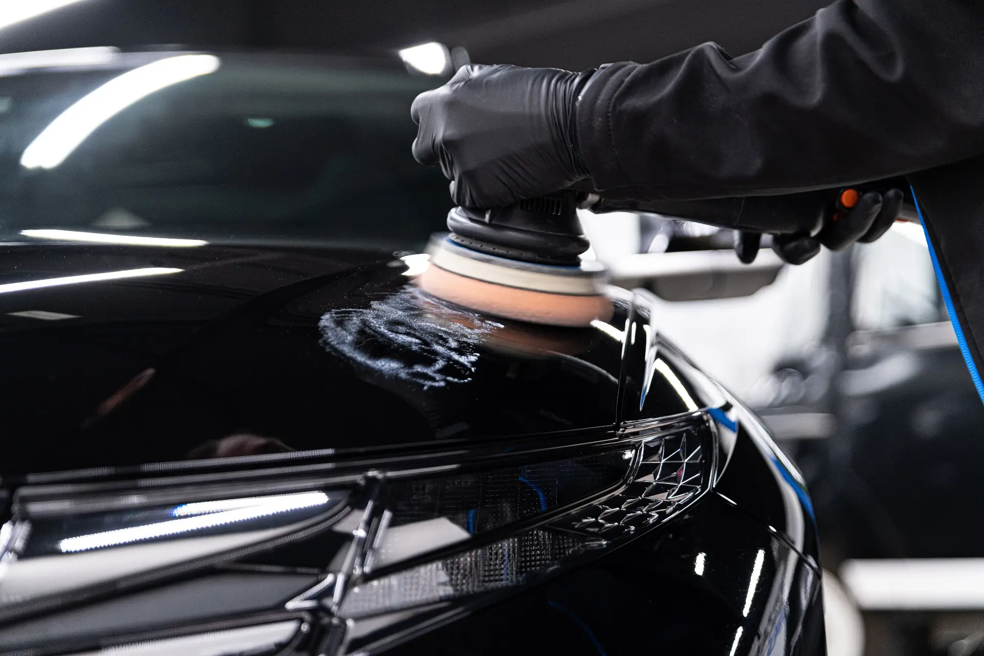 Detailer machine polishing the glossy black hood of a car
